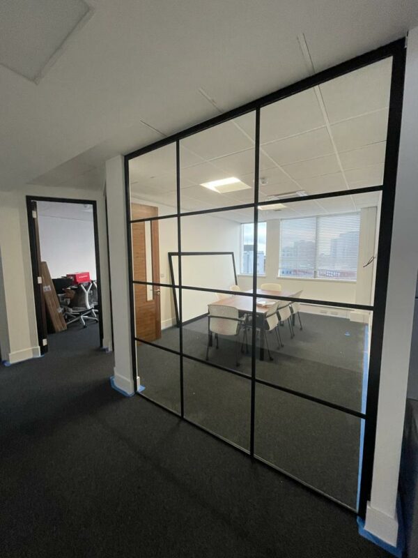 Meeting room created by single glazed glass partition in office with black banding strips