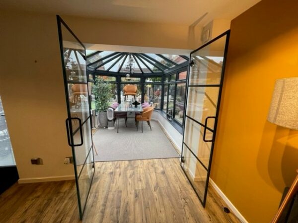 Open glass door partitions for the home on wooden flooring leading to conservatory